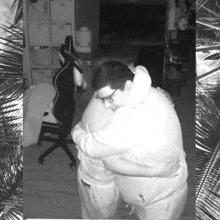 two men hugging in a room with a chair in the background