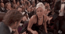 a woman in a black dress is kneeling down in front of a crowd of people .