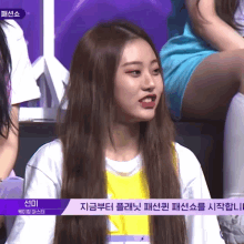 a girl with long brown hair is sitting in front of a sign that says ' snmi ' on it