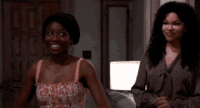 two women are dancing in a living room and one of them is looking at her phone