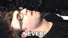 a man wearing glasses is laying down with the word never written on his face