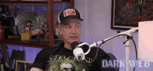a man is sitting in front of a microphone wearing a hat and a t-shirt that says ' dark web '