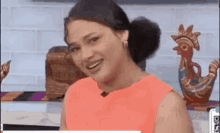 a woman in an orange dress is smiling while sitting on a chair in front of a rooster statue .