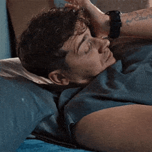 a man is laying on a bed with his head on a pillow and his hand on his forehead .