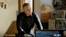 a man standing in front of a computer with a sign that says go on on the wall behind him