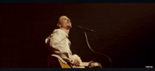a man singing into a microphone while playing a guitar in a vevo video