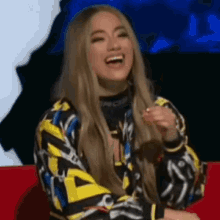 a woman with long blonde hair is sitting on a red couch laughing .