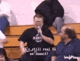 a man in a nasa shirt is holding a microphone and says it 's still real to me dammit