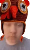 a person wearing a crocheted owl hat looks down