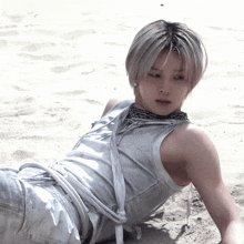 a man in a white tank top laying on the sand