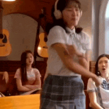 a girl in a school uniform is wearing headphones and dancing in a room .
