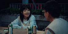 a man and a girl are sitting at a table with cans of beer .
