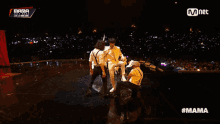 a group of men are dancing on a stage with the word mama on the bottom right