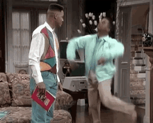 two men are dancing in a living room while a man holds a magazine .