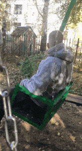 a man sits on a green swing with a gray hoodie on