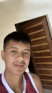 a young man in a red tank top is taking a selfie in front of a wooden door