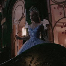 a woman in a blue dress is holding a wand and wearing a tiara