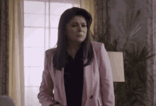 a woman in a pink jacket is standing in a living room next to a lamp .