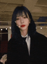 a girl with blue hair is wearing a suit and tie and has a microphone on her head .