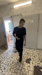 a man in a black shirt is walking down a hallway while holding a cell phone