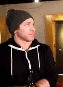 a man wearing a gray beanie and a black hoodie is holding a bottle of beer .