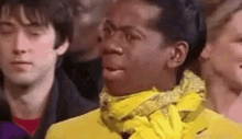 a man in a yellow jacket and scarf is making a funny face .