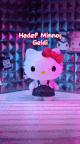 a hello kitty doll with a red bow is standing on a table in front of a pink wall .