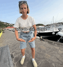 a woman wearing shorts and a white t-shirt stands in front of boats with the caption mec de cite simple