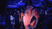 a man in an orange shirt with the letter e on it stands in a crowd of people