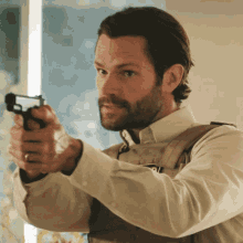 a man with a beard is pointing a gun with the letter p on his vest