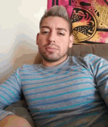 a man is sitting on a couch wearing a striped shirt and looking at the camera .
