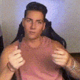 a man in a pink tank top is sitting in a chair holding a pen .
