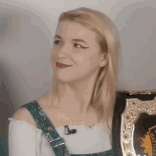a blonde woman wearing a white off the shoulder top with a green strap around her shoulder