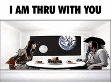 two women are sitting at a table with plates of food in front of a picture of the earth .