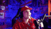a man in a red hat is holding a microphone in front of a wall with posters on it