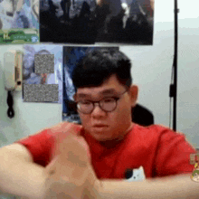 a man wearing glasses and a red shirt has his hands folded