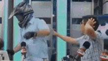 a man wearing a helmet is standing next to a man wearing a mask and holding his head .
