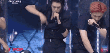 a man is singing into a microphone on a stage while another man watches .