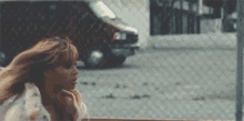 a woman with long hair is standing in front of a chain link fence with her hair blowing in the wind .