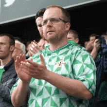a man wearing glasses and a green and white shirt is clapping his hands