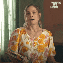 a woman in a floral shirt is holding a binder with the words " you 're my hero " on the bottom