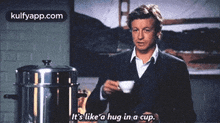 a man in a suit is holding a cup of coffee and says it 's like a hug in a cup