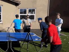 a group of people are playing ping pong in a backyard
