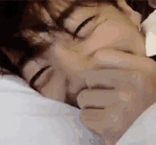 a close up of a person sleeping on a bed with their hands on their face .