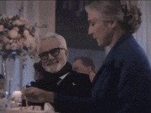 a man with a beard and glasses is standing next to a woman in a blue jacket