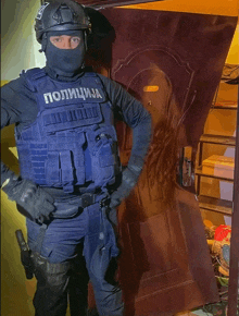 a police officer stands in front of a door wearing a blue vest that says policija