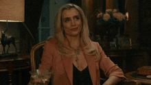 a woman in a pink jacket sits in a chair holding a martini