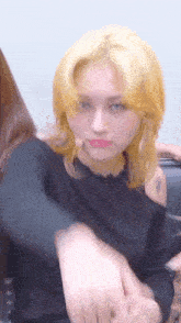 a woman with blonde hair and blue eyes is wearing a black sweater and making a funny face .