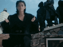 a woman in a black fur coat is standing on a rock wall .