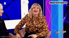 a woman is sitting in a chair laughing and pointing at something while another woman looks on .